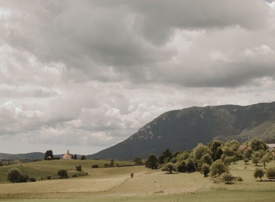 The photograph shows a karst landscape with green meadows and the Church of St George in Šmihel pod Nanosom near Postojna.