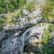 Two hikers walk along the path across the natural stone bridge in Rakov Škocjan.