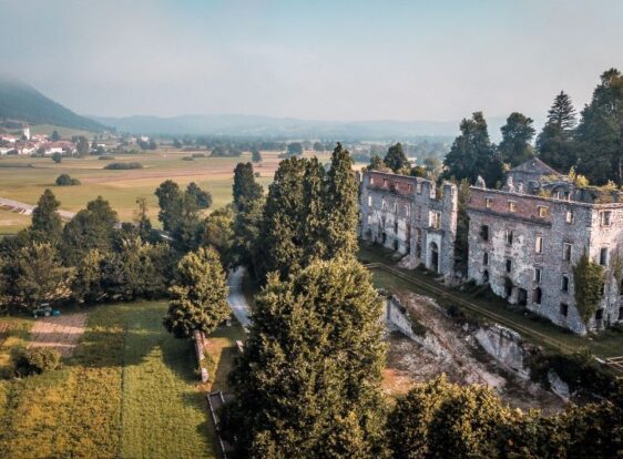 The photograph shows the ruins of Haasberg Castle (Hošperk), set against the distinctive landscape of Planina Polje.