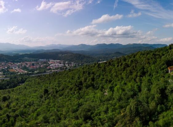 A view of Koča Mladika above the town of Postojna, with forested slopes in the foreground and the town nestled in the valley below.