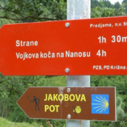 Dve usmerjevalni tabli. Ena je rdeča, druga pa rjave barve z napisom Jakobova pot in z znakom školjke.