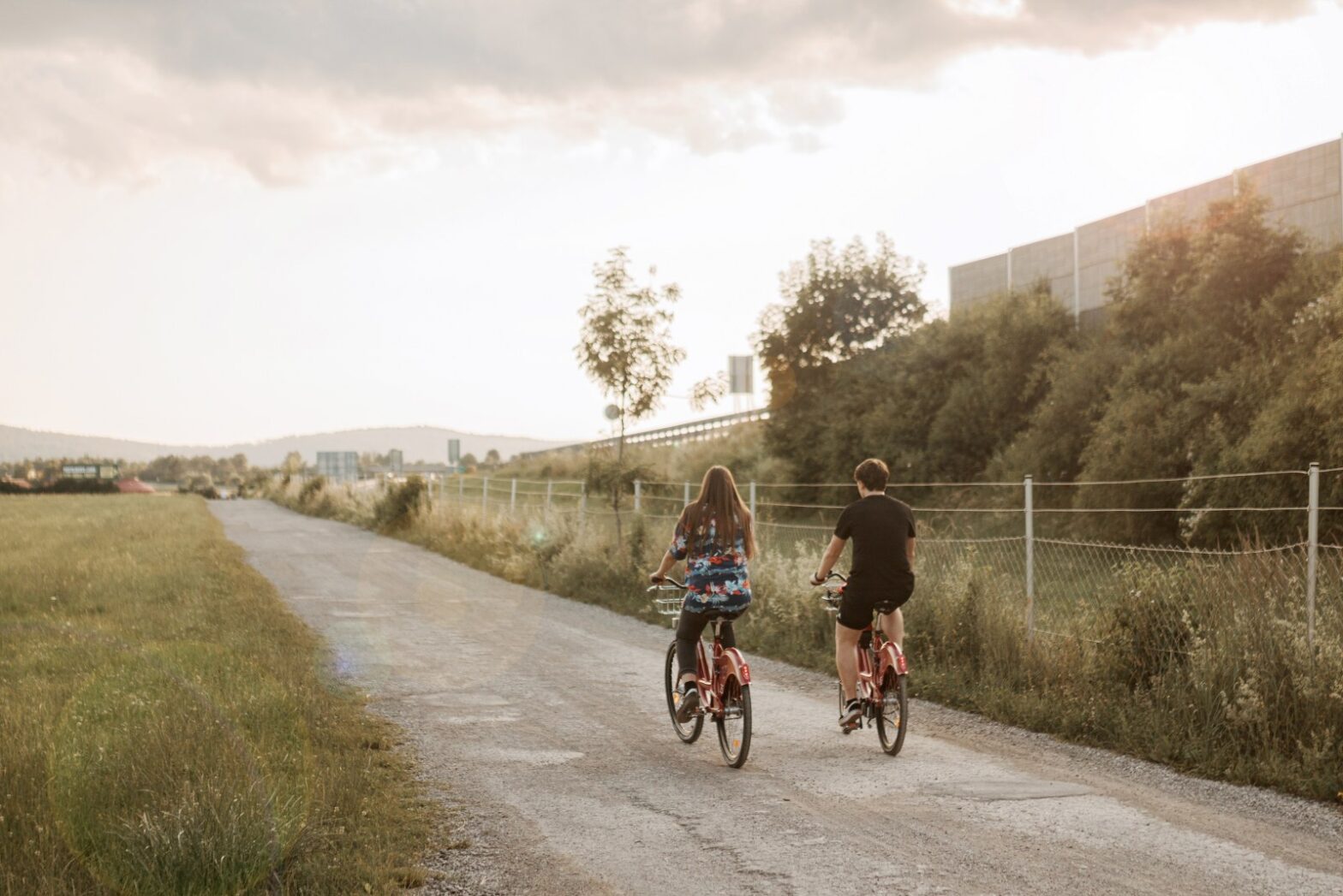 A girl and a boy cycling along a flat gravel road.