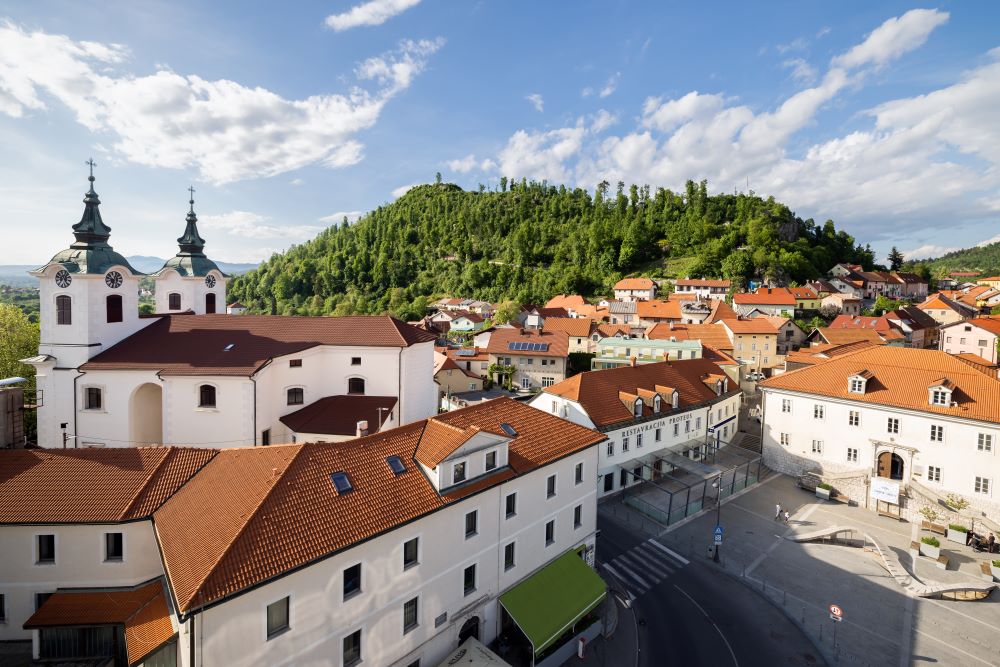 Pogled na mestni hrib Sovič, pod njim pa mestno jedro obdano s ključnimi zgradbami, ki pišejo zgodovino in sedanjost Postojnskega. Od Cerkve Svetega Štefana do mestnega trga in pogled na staro mestno jedro Majlont.