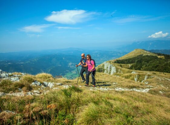 Two hikers walk along the ridge of Nanos, overlooking the valley and the surrounding mountain peaks.