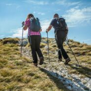 Two hikers make their way towards the summit of Nanos, carrying backpacks and using trekking poles as they approach the top.