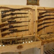 The photograph shows a display cabinet containing various historic firearms, hunting equipment, and other artefacts from the hunting collection. These exhibition pieces form part of the hunting collection at the Pri Stara dama Museum in Predjama.