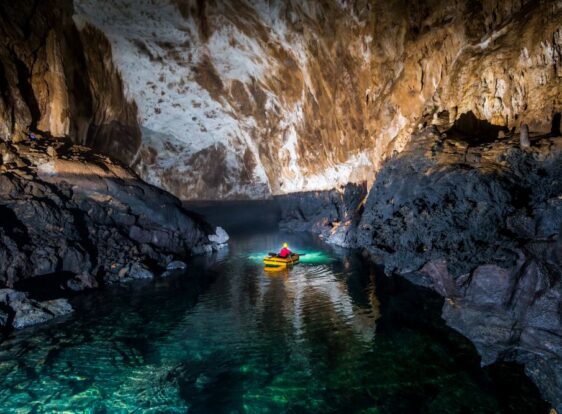 A caver, illuminated by a headlamp while navigating by boat, admires the wonders carved by water deep within the cave.