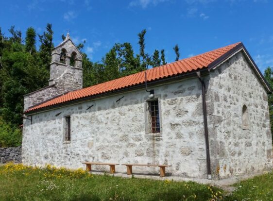 A small stone church with a red roof stands atop St Lovrenc Hill, surrounded by open meadows.
