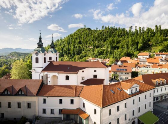 Panoramic view of Postojna’s historic town centre and Sovič Hill, rising above the town. In the foreground stands the Church of St Stephen.