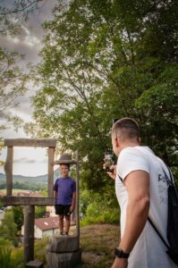Otrok pozira na leseni fototočki na Jakobovi poti, kjer je razgledna točka, medtem ko ga odrasla oseba fotografira.