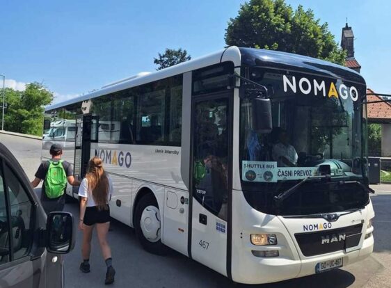 A shuttle bus connecting Postojna Cave and Predjama Castle. Two passengers are standing in front of the bus.